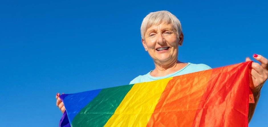 Close up portrait of a smiling older woman holding a Pride flag.