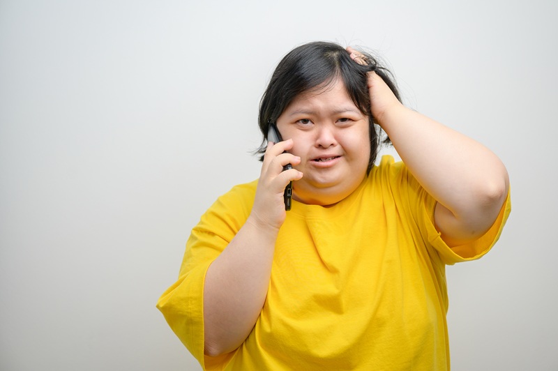Portrait of a woman with Down syndrome, talking on mobile phone with a worried and stressed expression, one hand on head, Down syndrome awareness, on a clean white background.